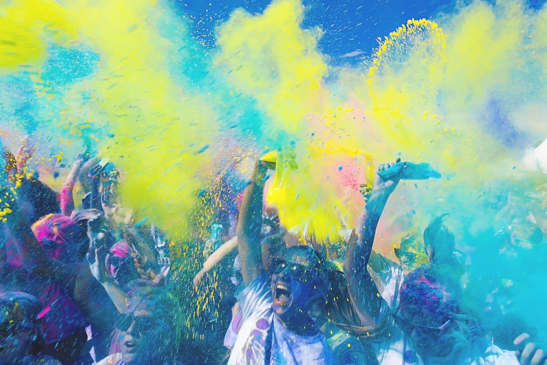 Festival crowd covered in clouds of yellow and blue colour powder