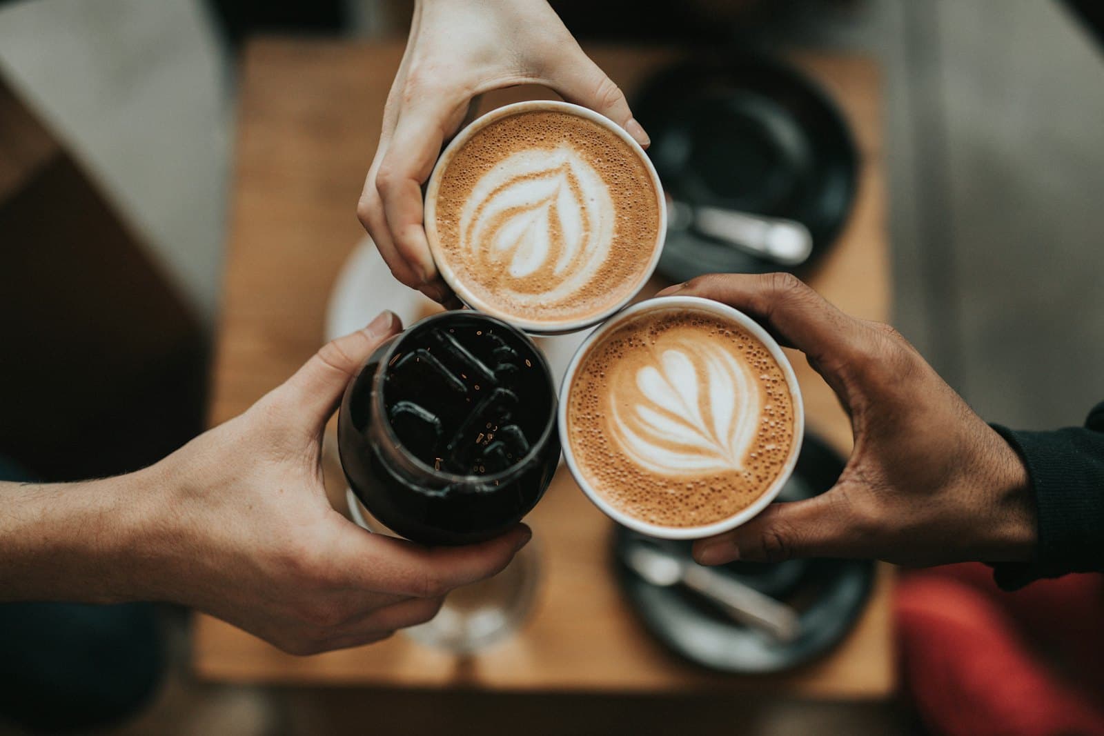 Friends clinking coffee cups with latte art over a café table