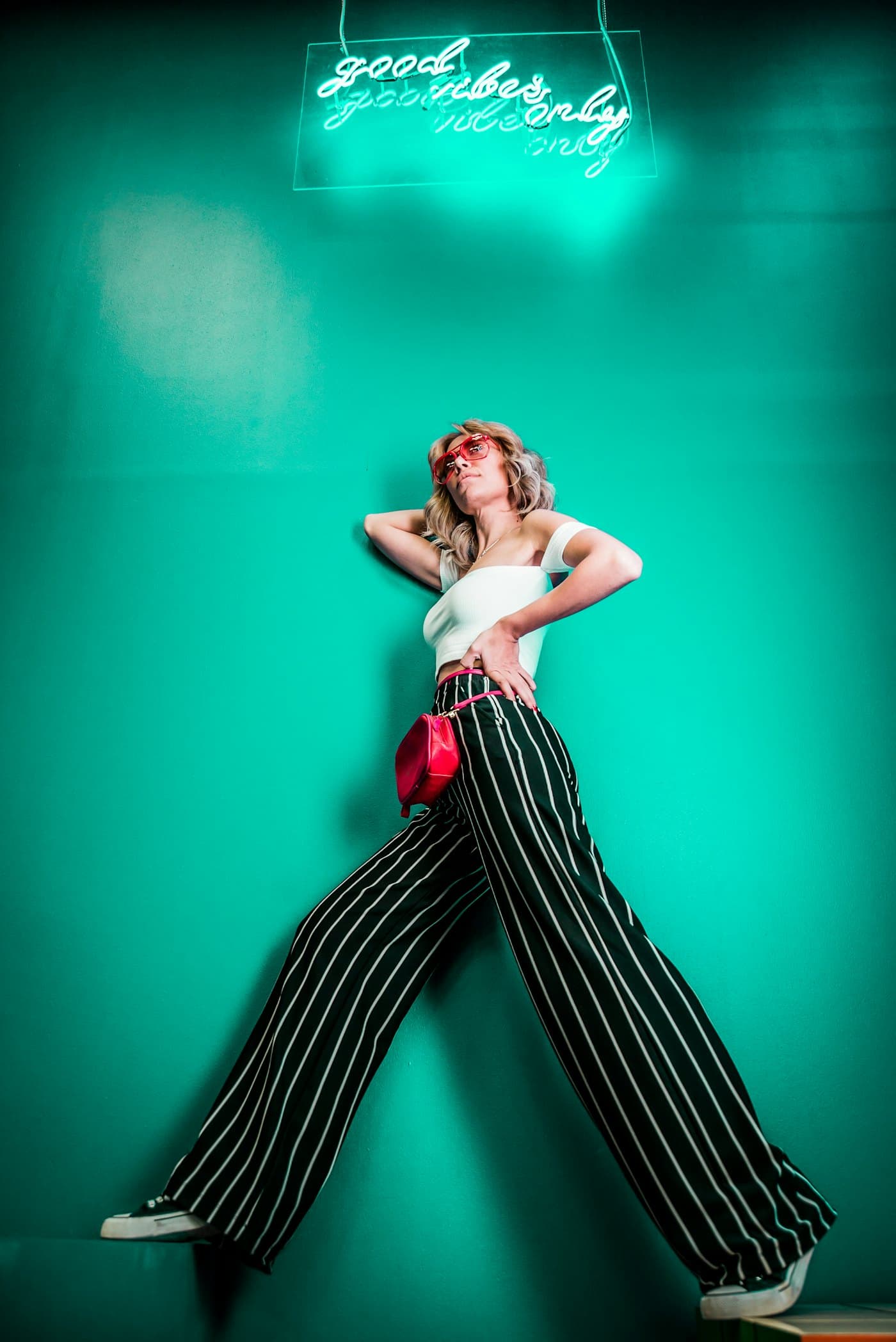 Model in striped trousers posing against a teal wall under a neon sign
