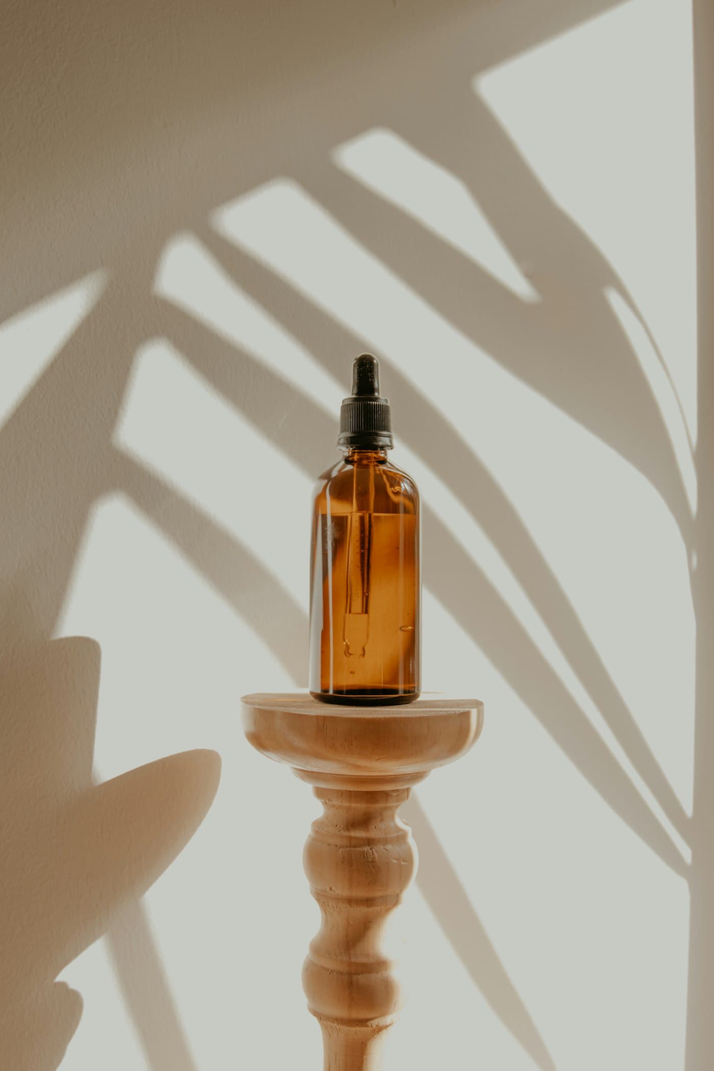 Amber dropper bottle on a turned wooden plinth with palm-leaf shadows