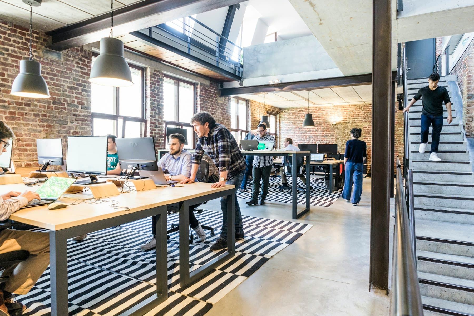 Open-plan loft studio with long desks, pendant lamps and a staircase